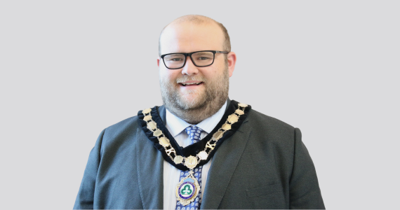 A smiling man in a suit wearing a chain of office. 