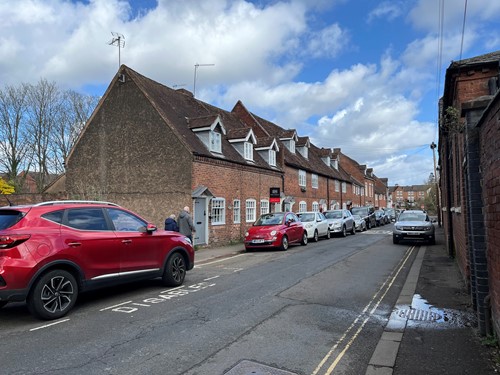 terraced dormer houses on narrow road with parked cars out front