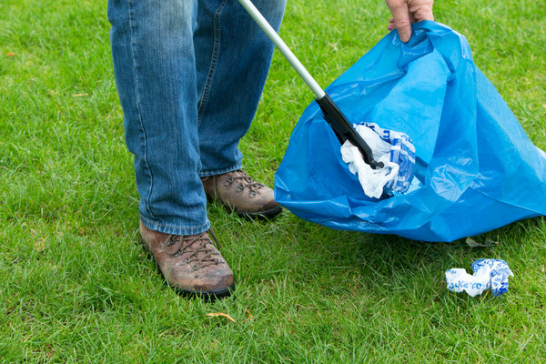 person holding a litter picker and rubbish bag, collecting litter from grass