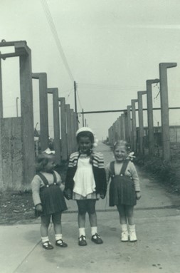 3 children in dresses at end of  concrete path with concrete uprights behind them