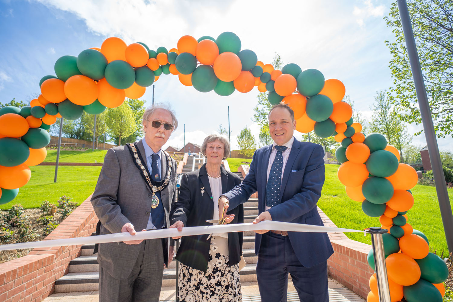 Three people stood under a balloon arch as part of a ribbon cutting ceremony