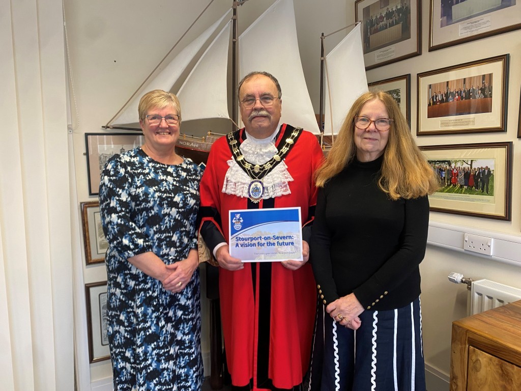 3 people smiling at camera man in centre in mayoral robes holding printed document