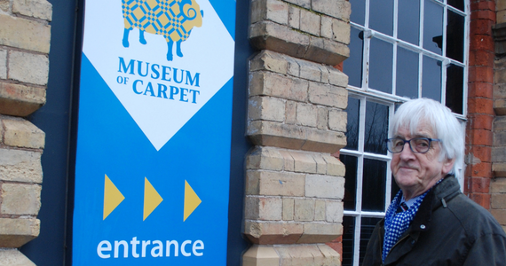 Man with white hair stood next to sign which says Museum of Carpet
