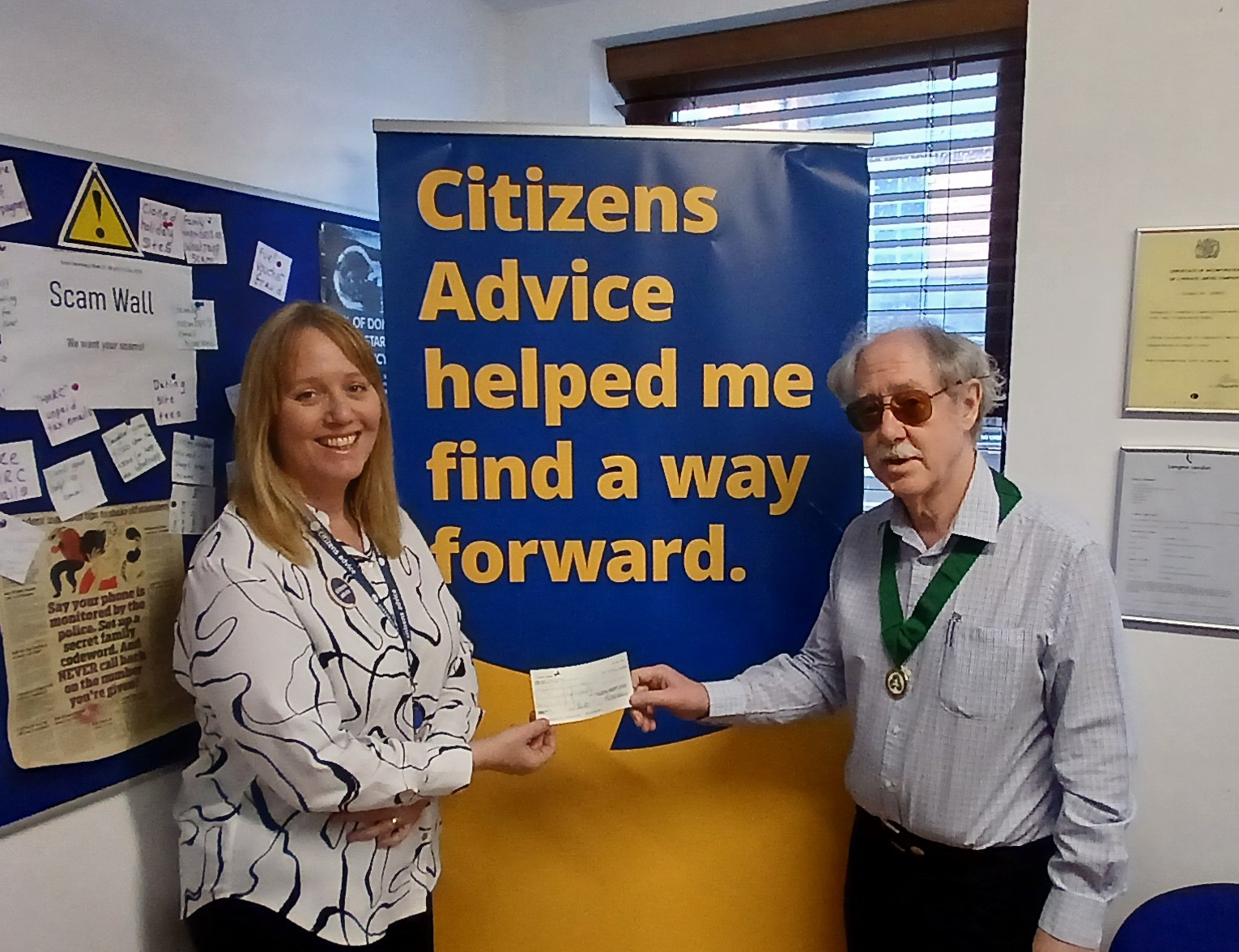 Older man wearing ceremonial chain presenting cheque to a lady.
