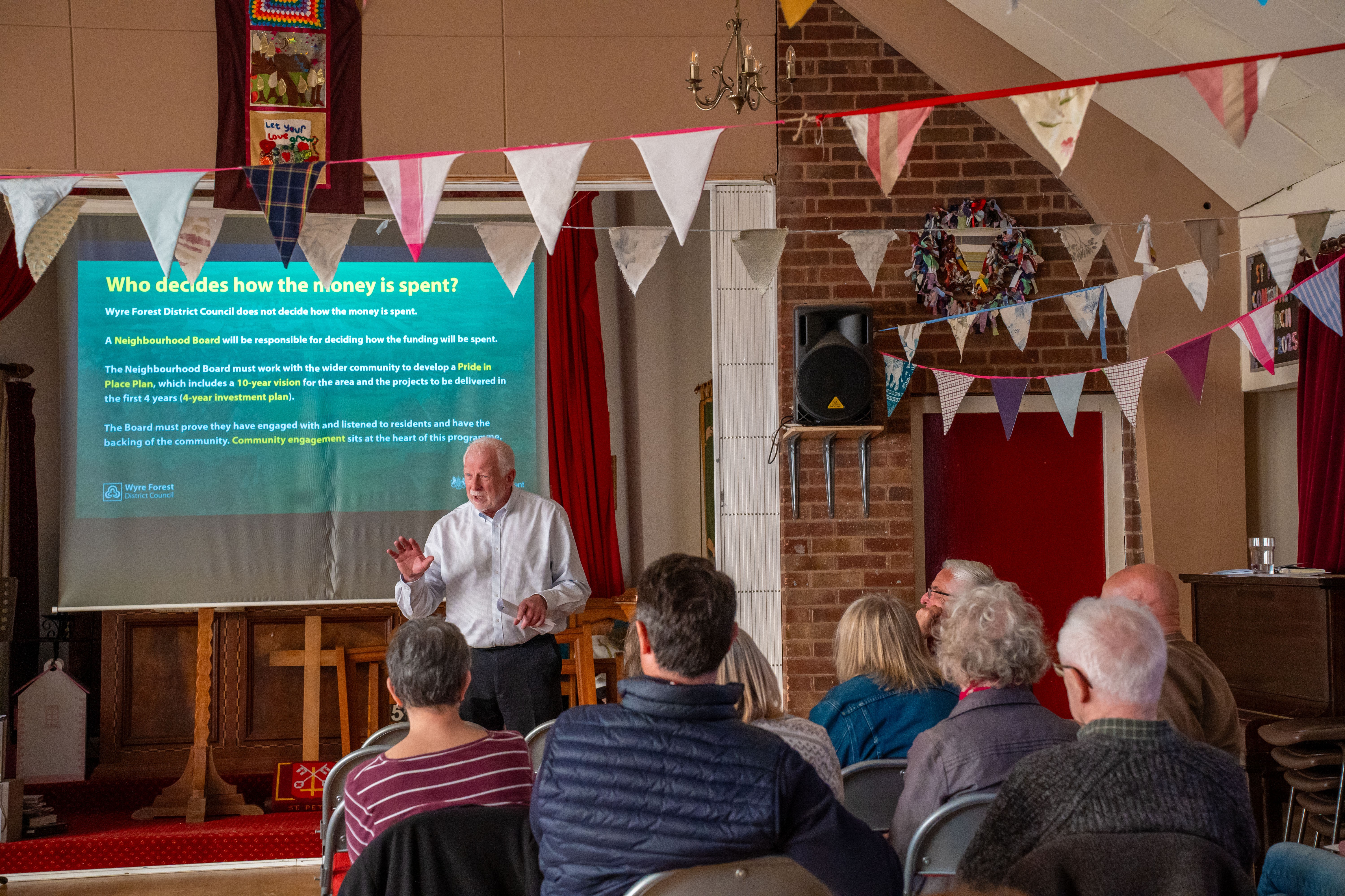 Man in foreground talking to a room of people with a flip chart in the background