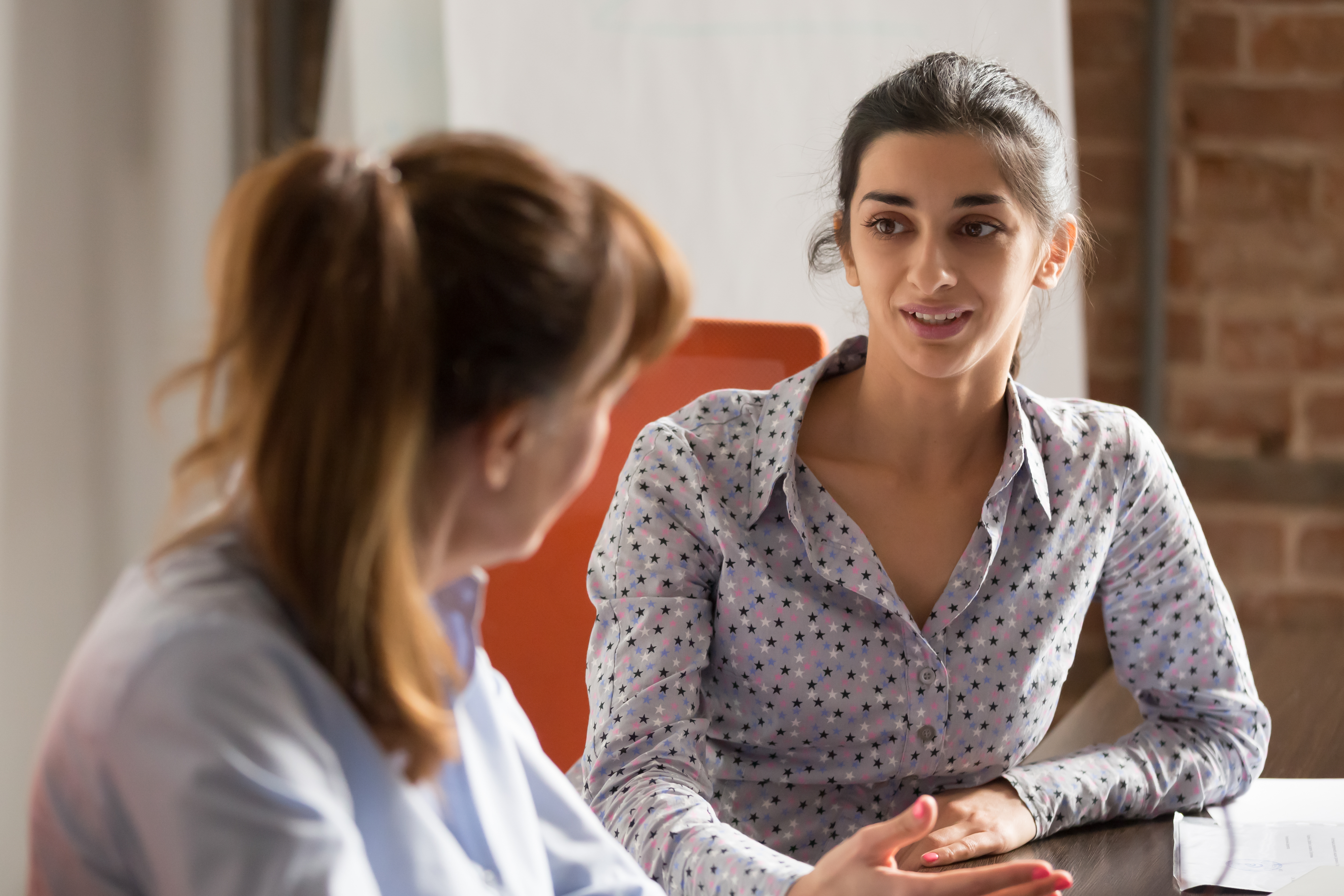 two female colleagues sat at desk talking